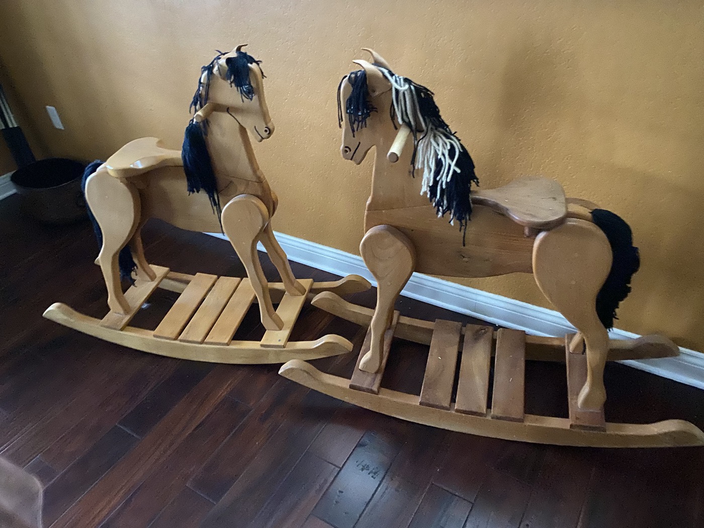 Two handcrafted wooden rocking horses with yarn manes side by side